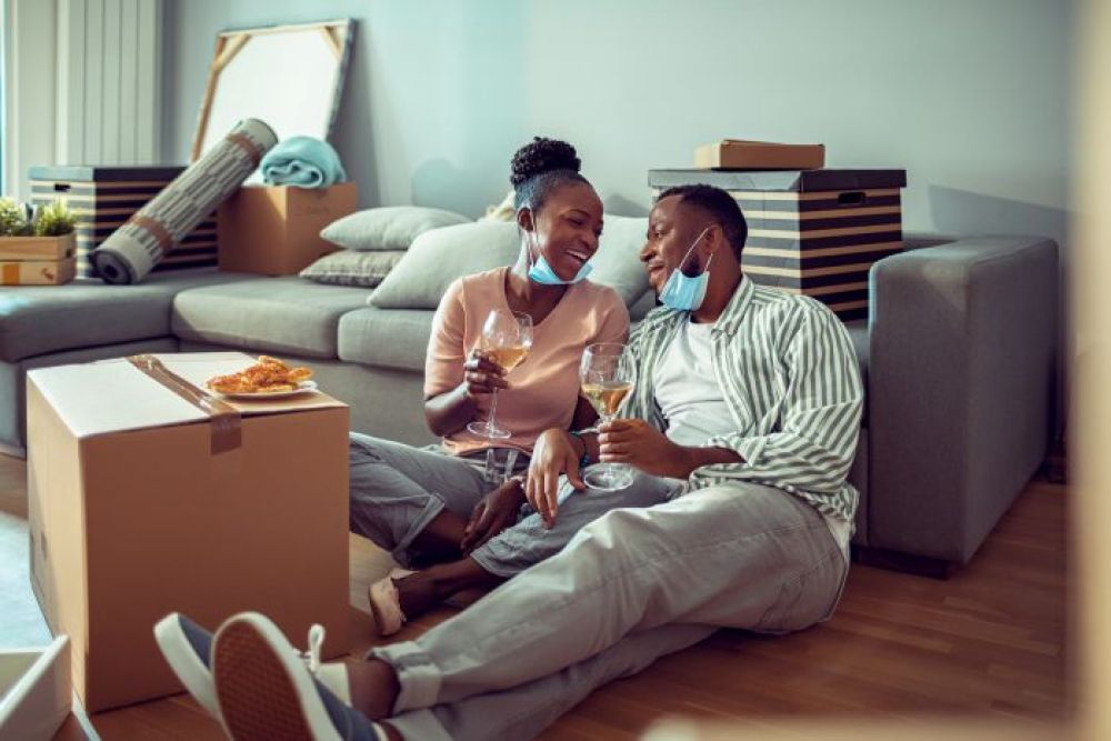 Couple sitting among moving boxes, toasting with wine glasses