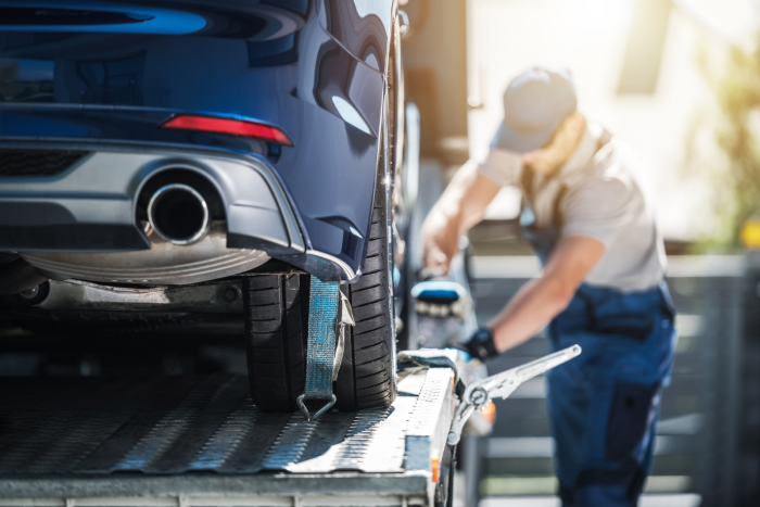 Worker securing a car with tie-down straps on an open transport trailer