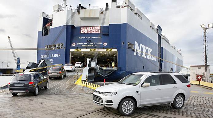 Rows of cars parked at a port terminal waiting to be loaded onto a ship