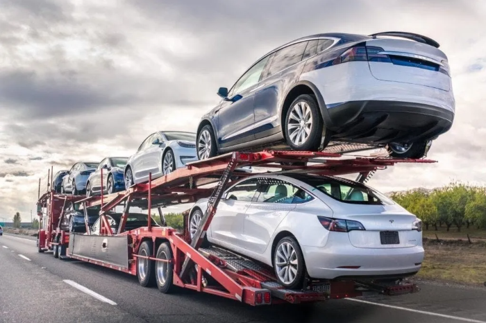 Open car carrier trailer hauling several cars and an SUV down a highway, the most common way to ship a car