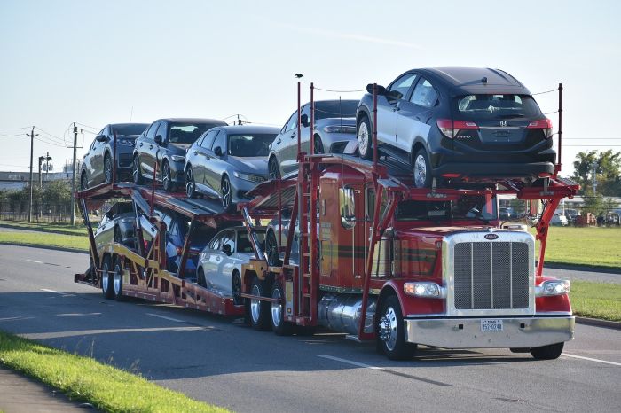 Open car carrier trailer hauling several vehicles down a highway