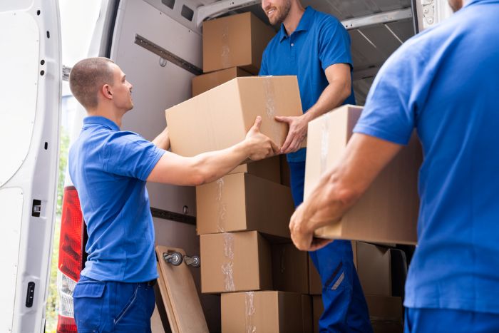 Movers in blue uniforms loading boxes into a moving van