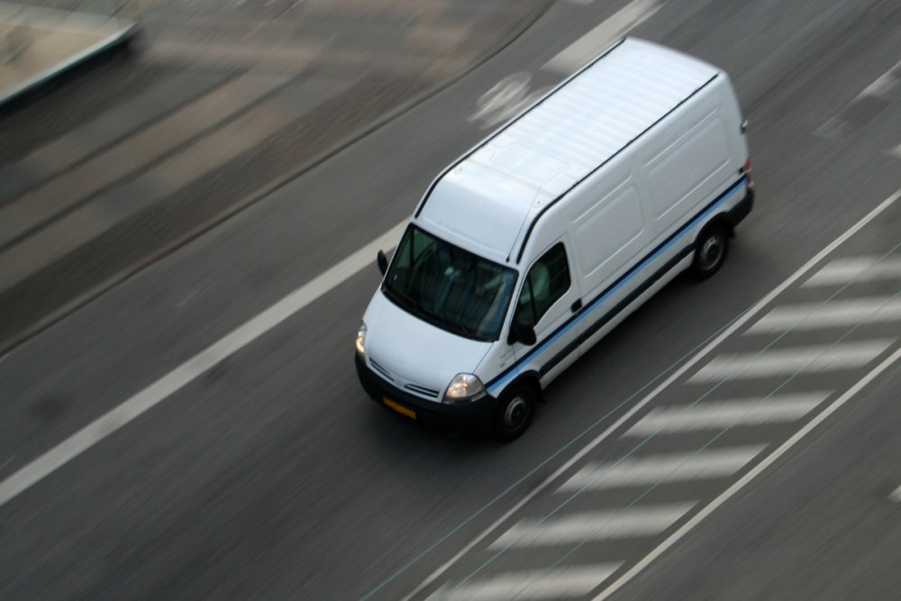 A small cargo moving van drives on a lined road.